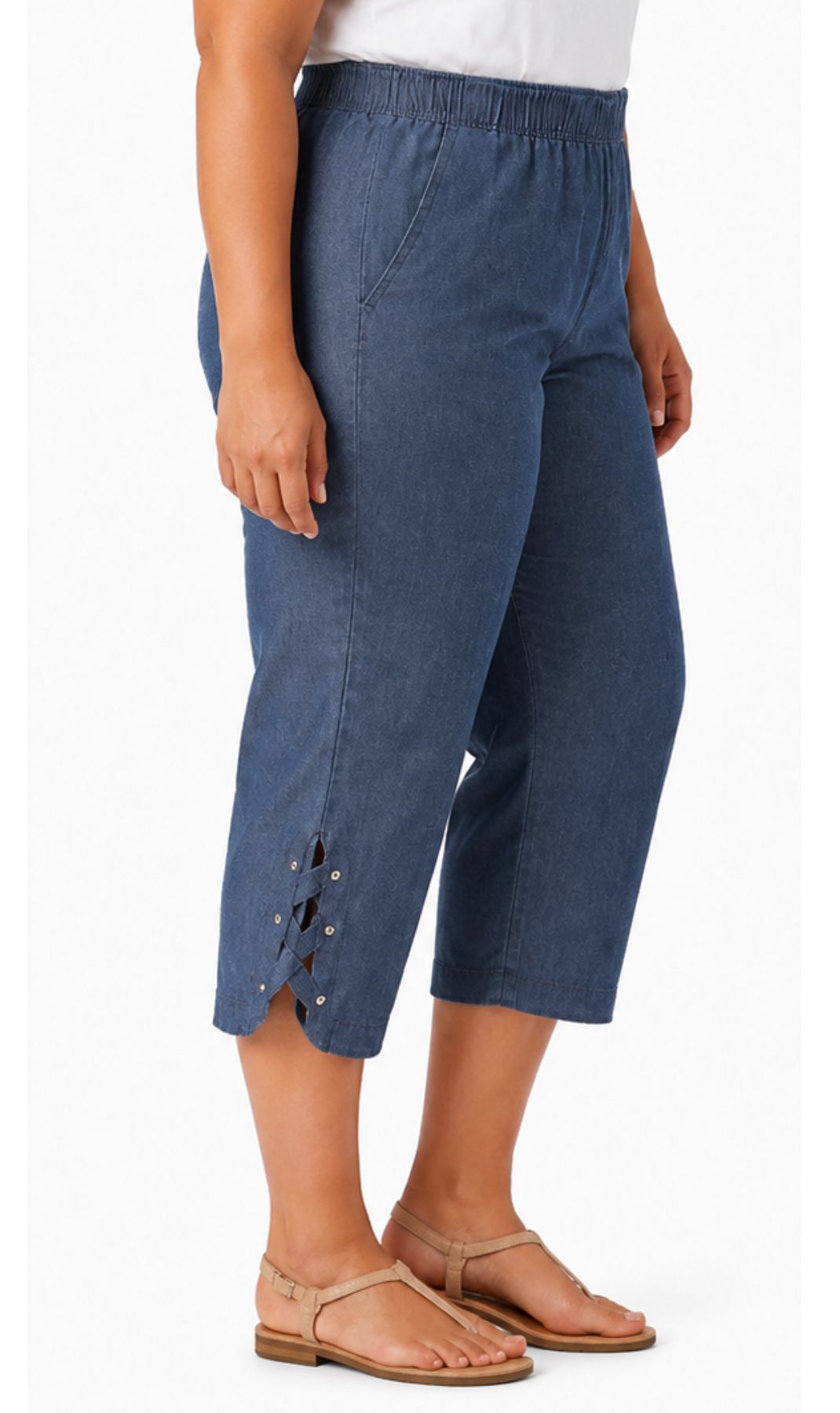A model wearing blue cropped pants with side cutouts and lace-up detailing, paired with tan flat sandals against a plain white background.