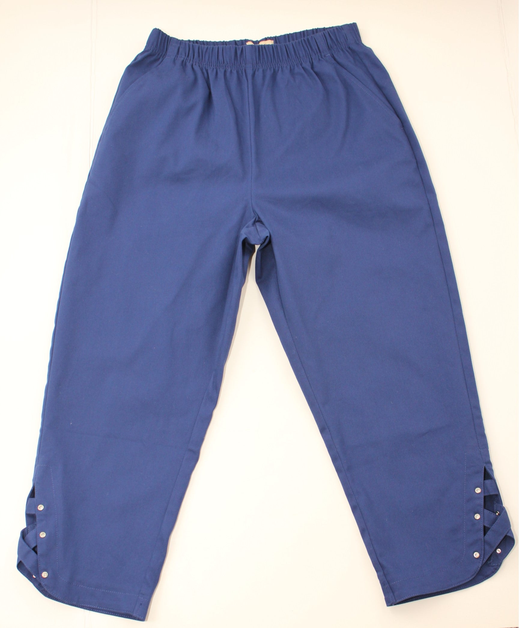 A pair of blue cropped pants with an elastic waistband and decorative cutout details on the lower hems, laid flat against a light background.