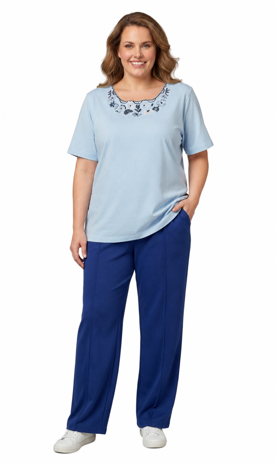 Woman wearing a light blue top with embroidery and dark blue pants on a white background